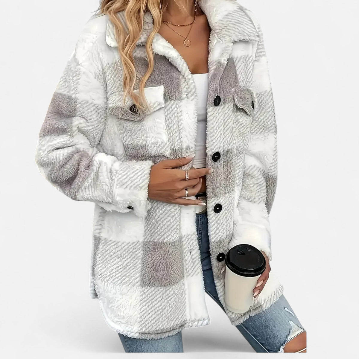 A woman wearing a white and grey plaid teddy fleece jacket over a white top and blue jeans, holding a coffee cup.