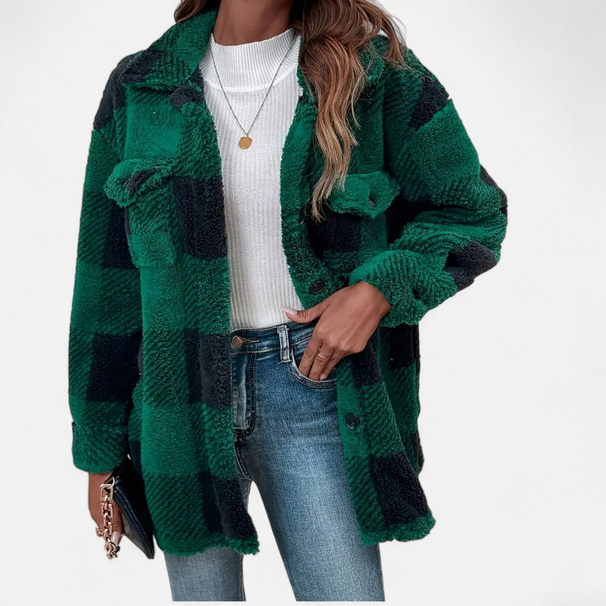 A woman wearing a dark green-and-black buffalo plaid teddy fleece jacket open over a white top and blue jeans.