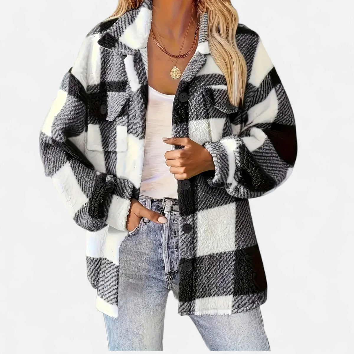A woman wearing an oversized black-and-white buffalo plaid teddy fleece shirt jacket with flap chest pockets and a button front, styled open over a white scoop-neck top and light-wash blue jeans.