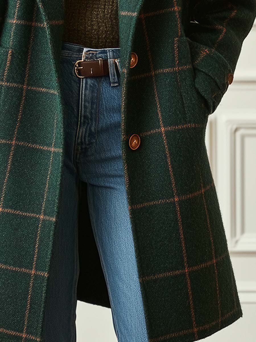 Close-up shot showing the side welt pocket, brown button closure, and windowpane plaid pattern of the dark green tweed coat paired with denim jeans.