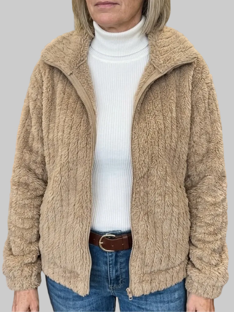 A woman wearing an open taupe ribbed fleece zip-up jacket with a fold-over collar over a white turtleneck top and blue jeans.