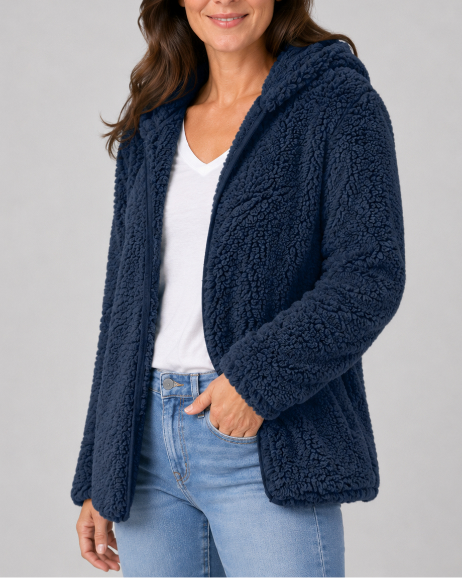A woman wearing an open navy blue hooded teddy fleece jacket over a white v-neck t-shirt and light blue jeans.
