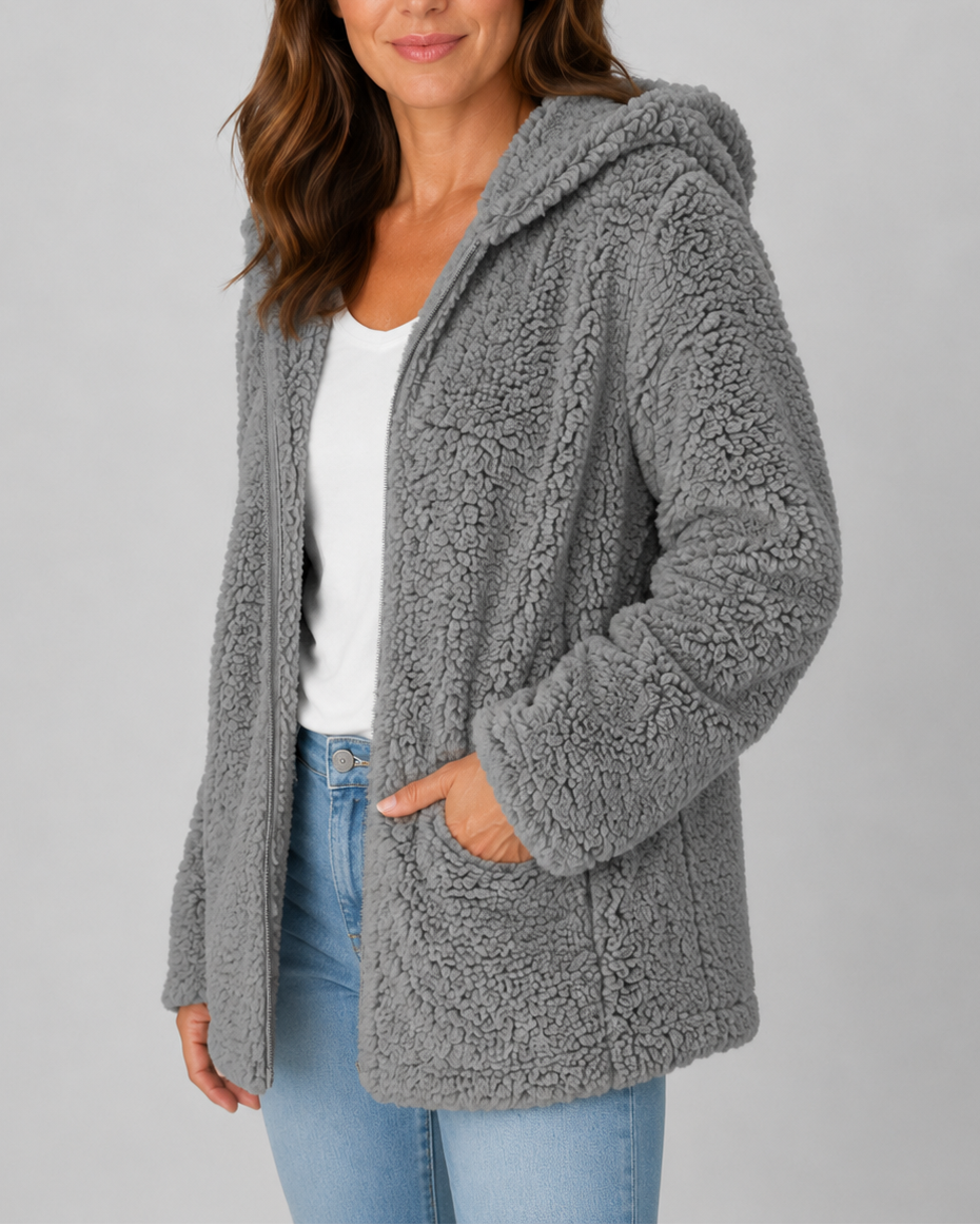 A woman wearing an open dark gray hooded teddy fleece jacket with front patch pockets over a white top and blue jeans.