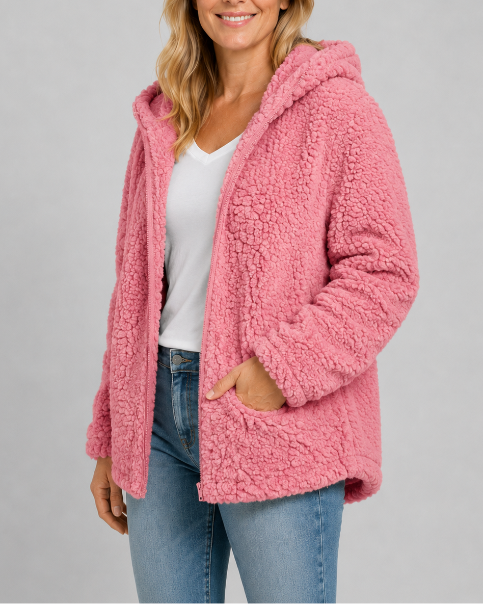 A woman wearing a soft medium pink hooded teddy fleece jacket layered over a white t-shirt and blue jeans.