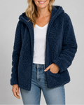 A woman smiling while wearing a navy blue hooded teddy fleece jacket open over a white v-neck shirt and light-wash blue jeans, with one hand in her pocket.