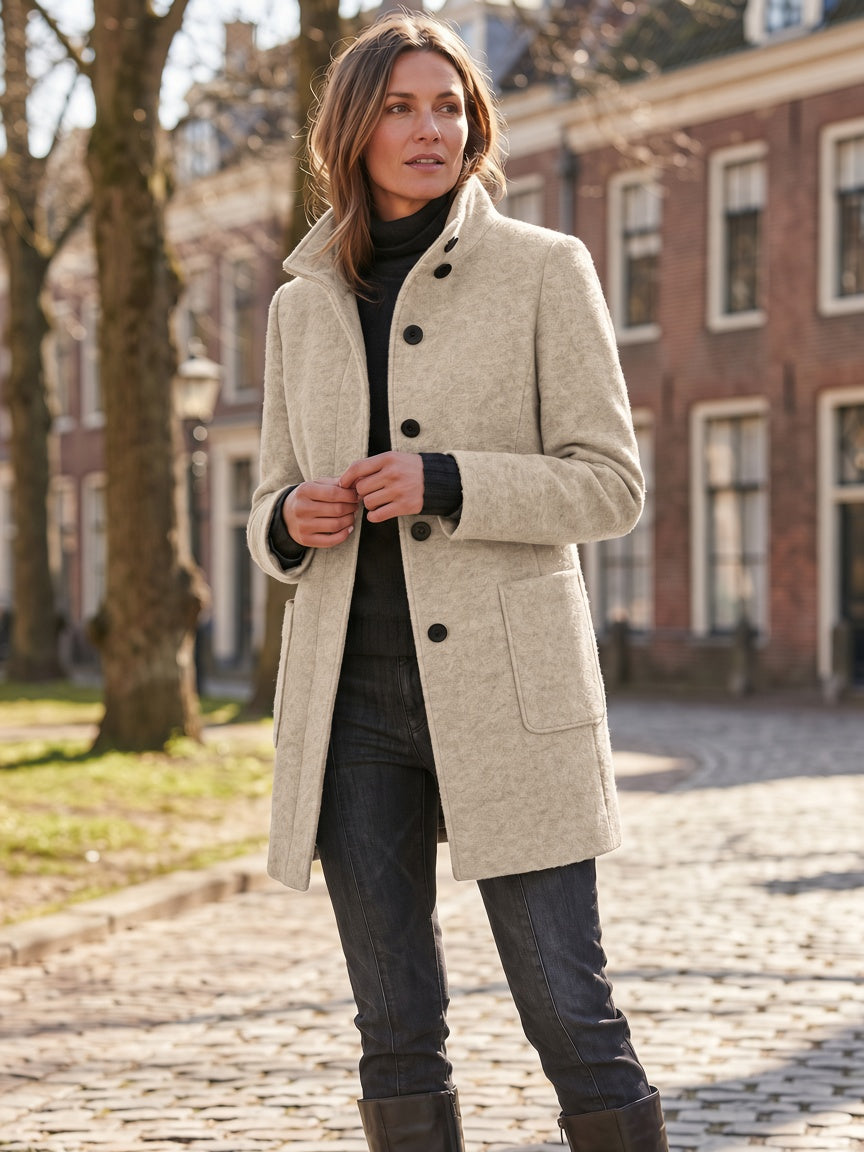 Three-quarter street style portrait of a model wearing the women's wool-blend coat in light oatmeal beige with contrast black front buttons and stand collar.