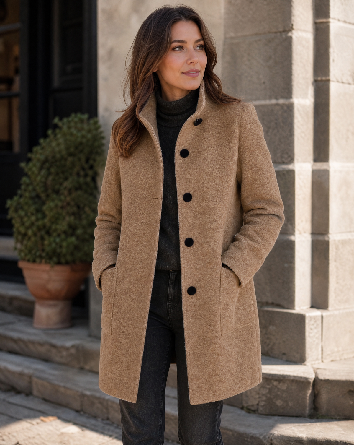 Three-quarter street style view of a model wearing the camel wool coat buttoned up with a high stand collar and patch pockets.