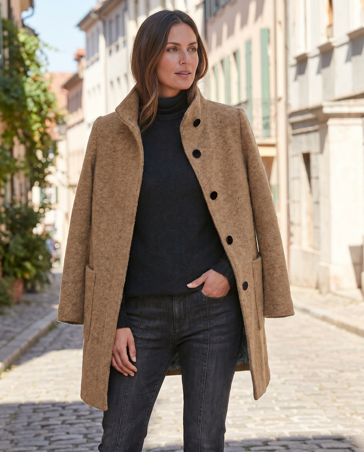 Three-quarter outdoor view of a model wearing the camel wool coat styled open over a black turtleneck sweater and jeans.