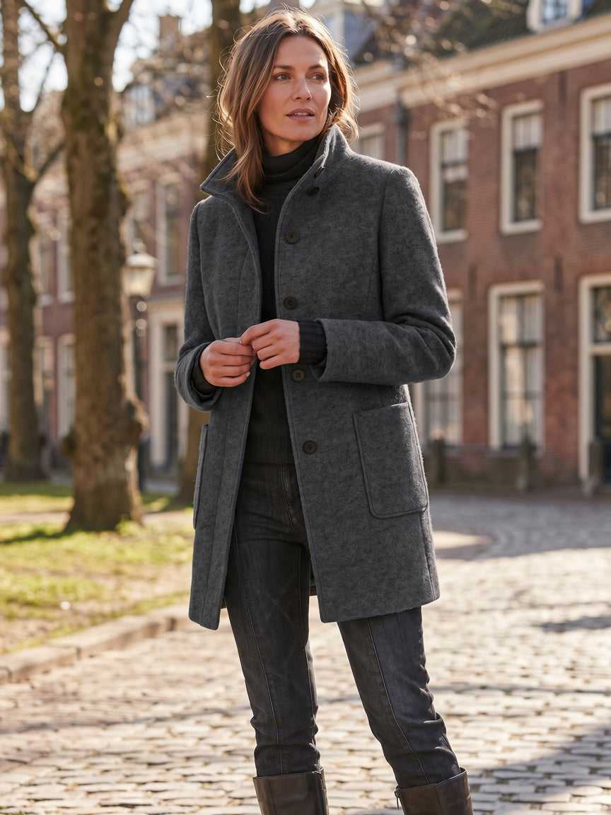 Three-quarter street view of a model wearing the dark charcoal gray wool-blend stand-collar coat buttoned up.