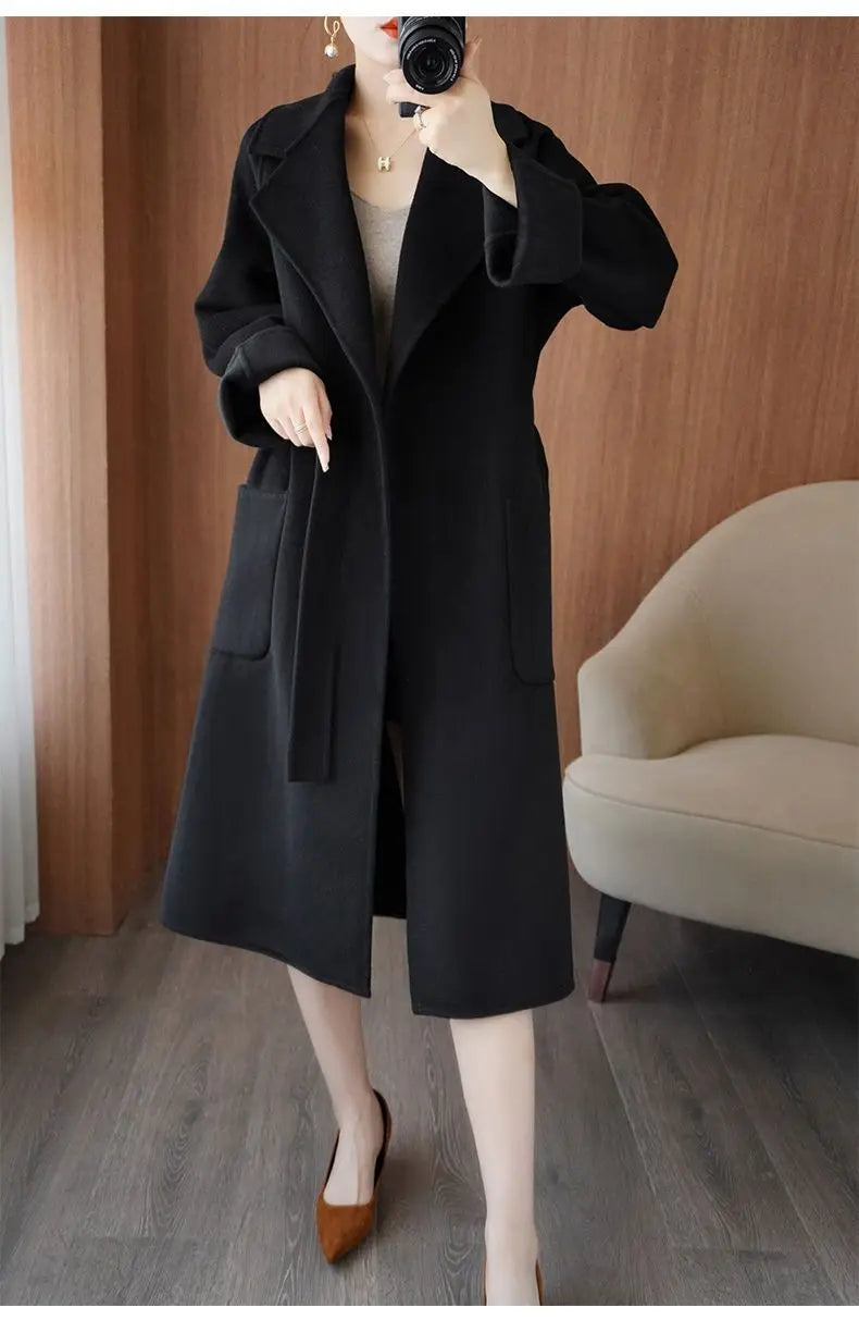 Full-length view of a woman wearing a black longline wool-blend coat tied tightly at the waist with a fabric belt, paired with brown pumps.