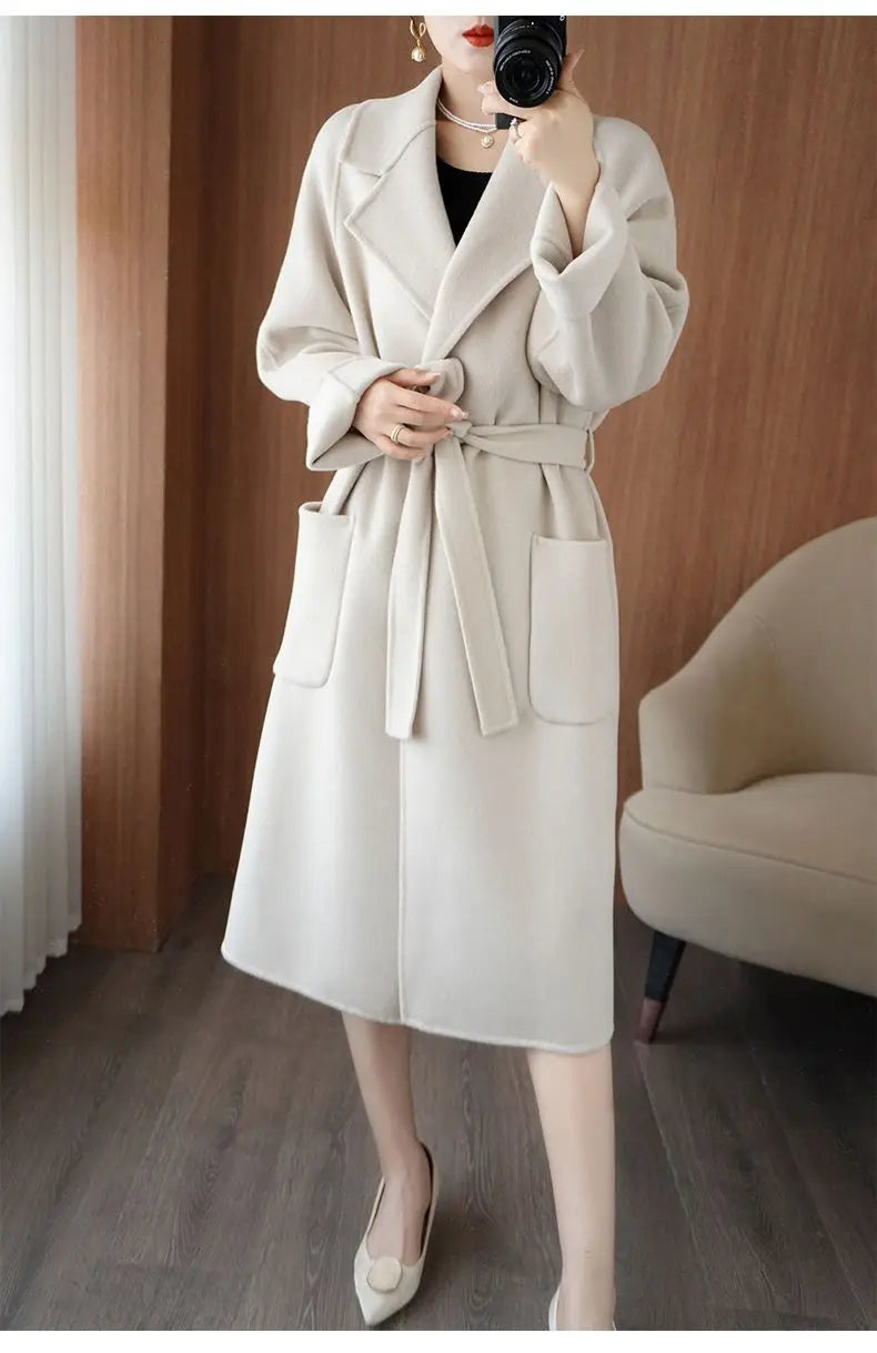 Full-length mirror selfie of a woman wearing a cream off-white longline wool-blend coat styled with a tied waist belt and front patch pockets[cite: 11].