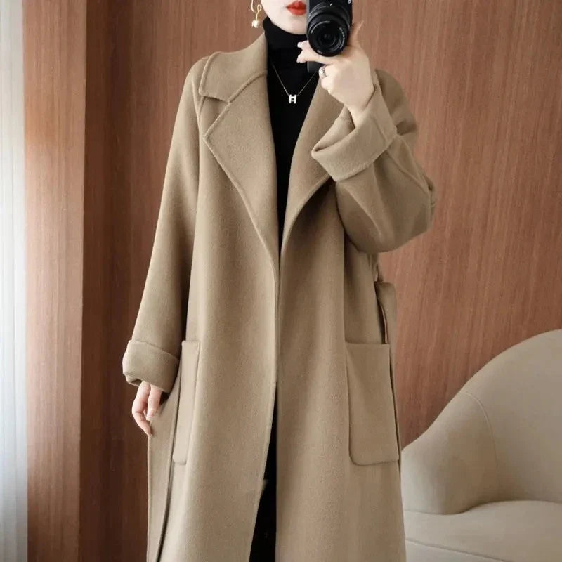 Mirror selfie close-up of a woman wearing an open taupe beige longline wool-blend coat over a black top.