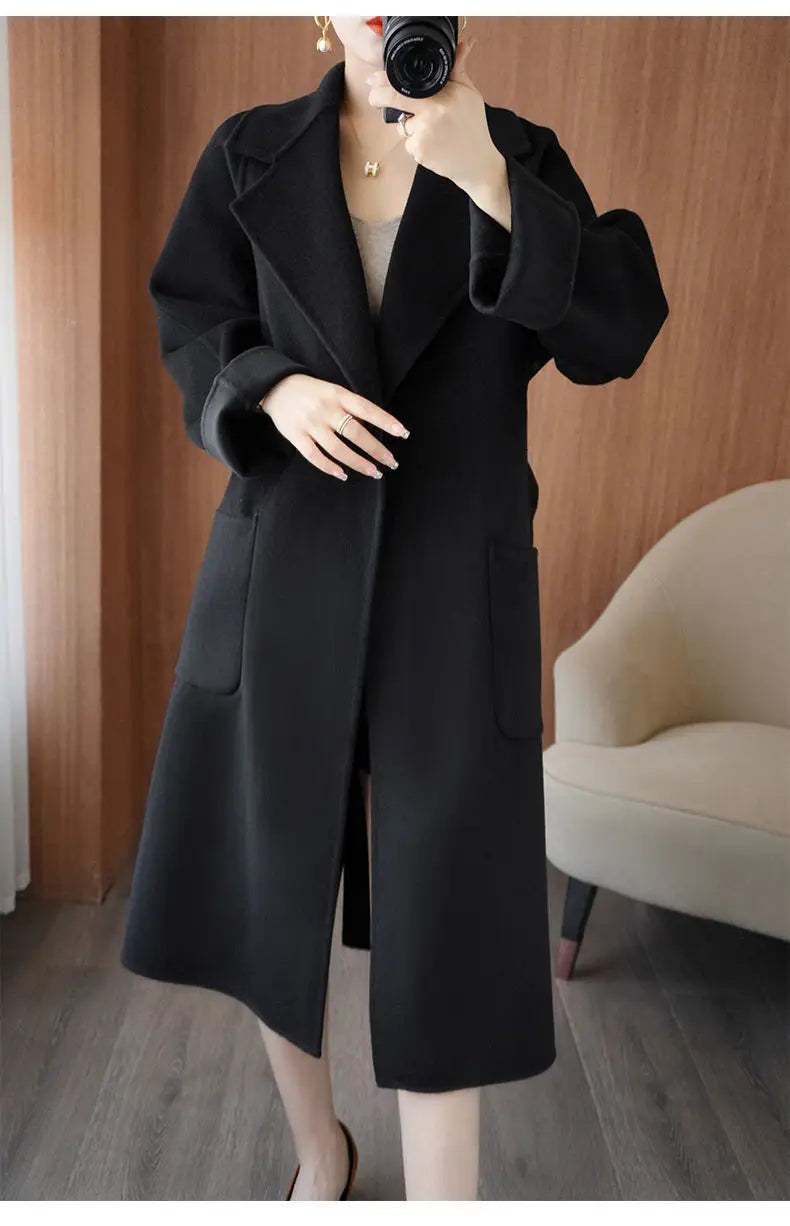 Full-length mirror selfie of a woman wearing an open black longline wool-blend coat featuring wide notch lapels and deep patch pockets.