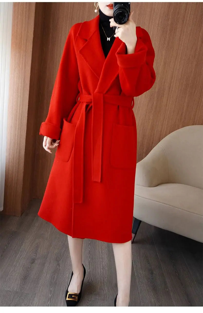 Woman taking a mirror selfie wearing a vibrant red longline wool-blend overcoat with wide notch lapels, large front patch pockets, and a matching tie belt at the waist, styled over a black turtleneck sweater and black high heels.