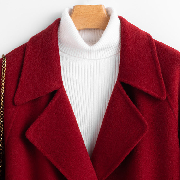 Close-up shot of the collar and neckline of the red wool coat, showing the wide notched lapels and white ribbed turtleneck inner layer.