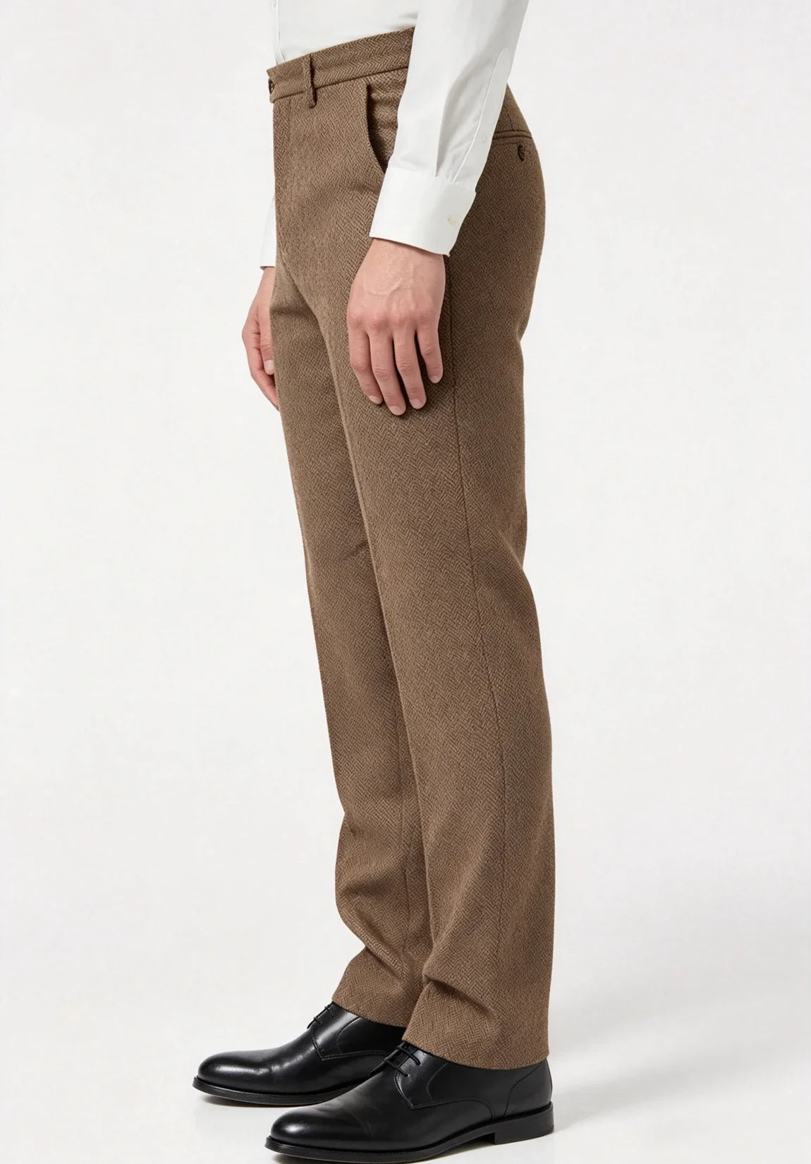 Full-length side profile view of a man wearing brown wool herringbone dress pants, a white dress shirt, and black dress shoes against a plain white studio backdrop.