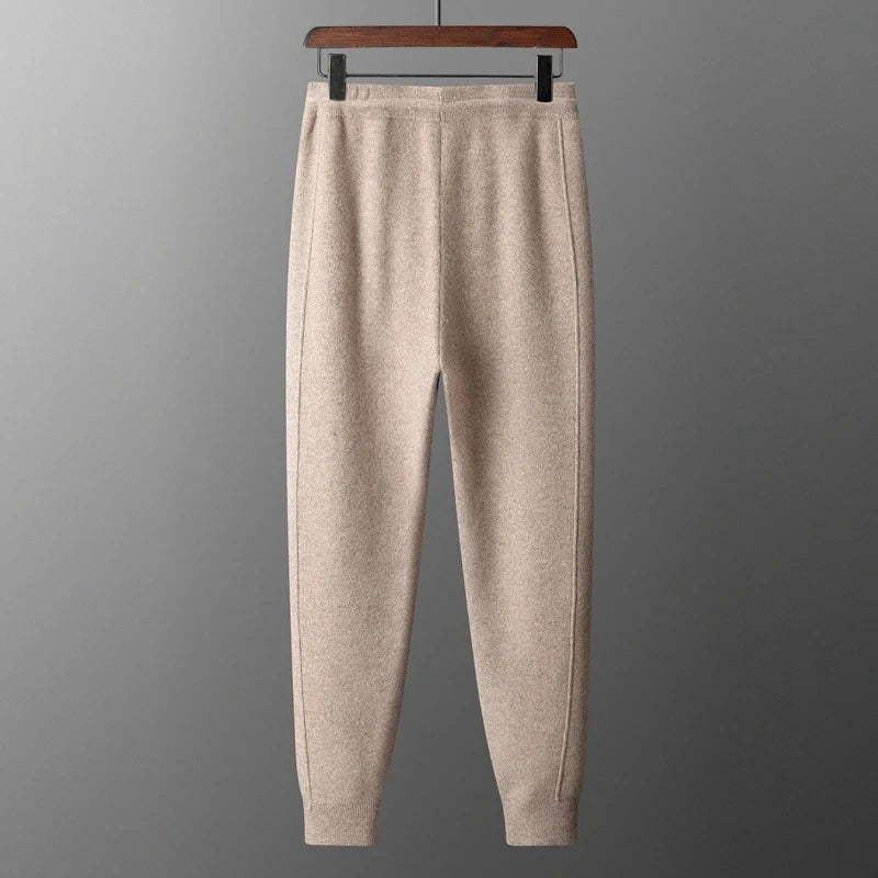 Full front view of beige oatmeal tapered wool knit sweatpants displayed on a hanger against a grey background.