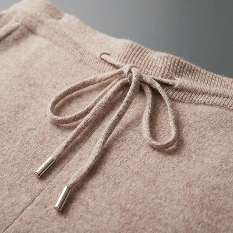 Close-up detail of the ribbed elastic waistband with a tied drawstring featuring metal aglet tips on beige wool knit fabric.