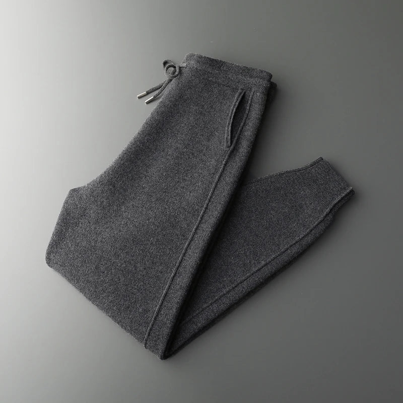 Neatly folded dark charcoal gray wool knit sweatpants displayed against a grey background.