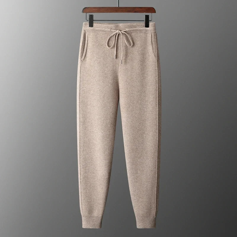 Front view of high-waisted beige oatmeal wool knit sweatpants hanging on a hanger, featuring an adjustable drawstring waistband, side slant pockets, and ribbed tapered cuffs.