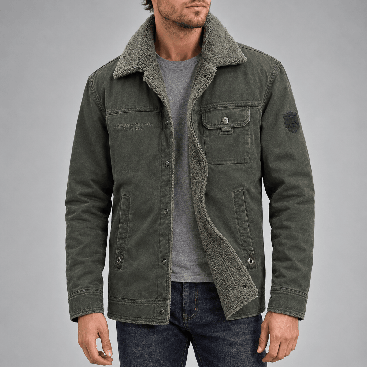Front view of a model wearing an open olive green wool-lined utility jacket with a grey sherpa-textured collar, single button flap chest pocket, side hand pockets, and inner plush lining over a grey shirt.