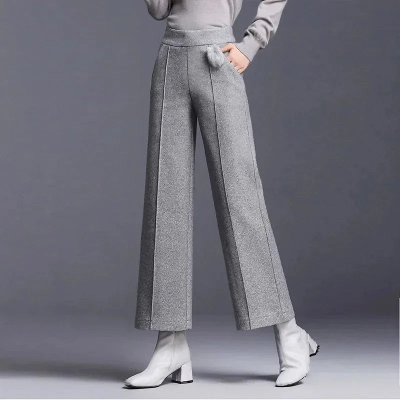 Alternate front view of the high-rise gray wool wide-leg trousers with front seams and side pocket detail, styled with white boots.