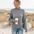 Grey chunky knit turtleneck sweater with balloon sleeves and an oversized, relaxed fit, worn on a sandy beach.