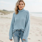 Light blue chunky knit turtleneck sweater with balloon sleeves and an oversized fit, worn on a beach.