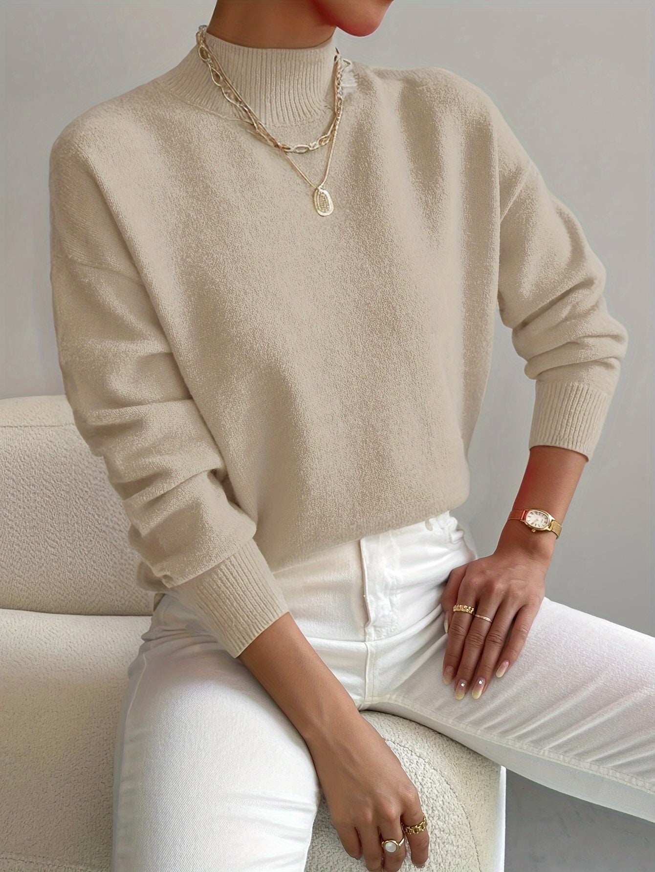 Beige ribbed turtleneck sweater with dropped shoulders and fitted cuffs, styled with white trousers.