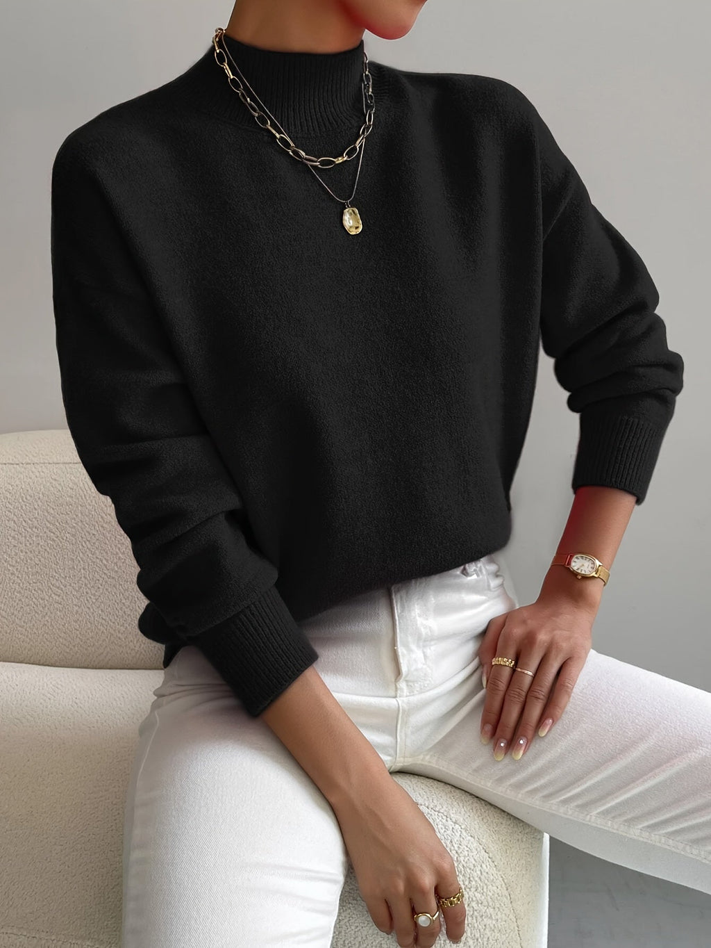 Black ribbed knit turtleneck sweater with dropped shoulders, long sleeves, and fitted cuffs worn with white jeans.