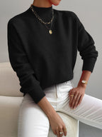 Black ribbed knit turtleneck sweater with dropped shoulders, long sleeves, and fitted cuffs worn with white jeans.