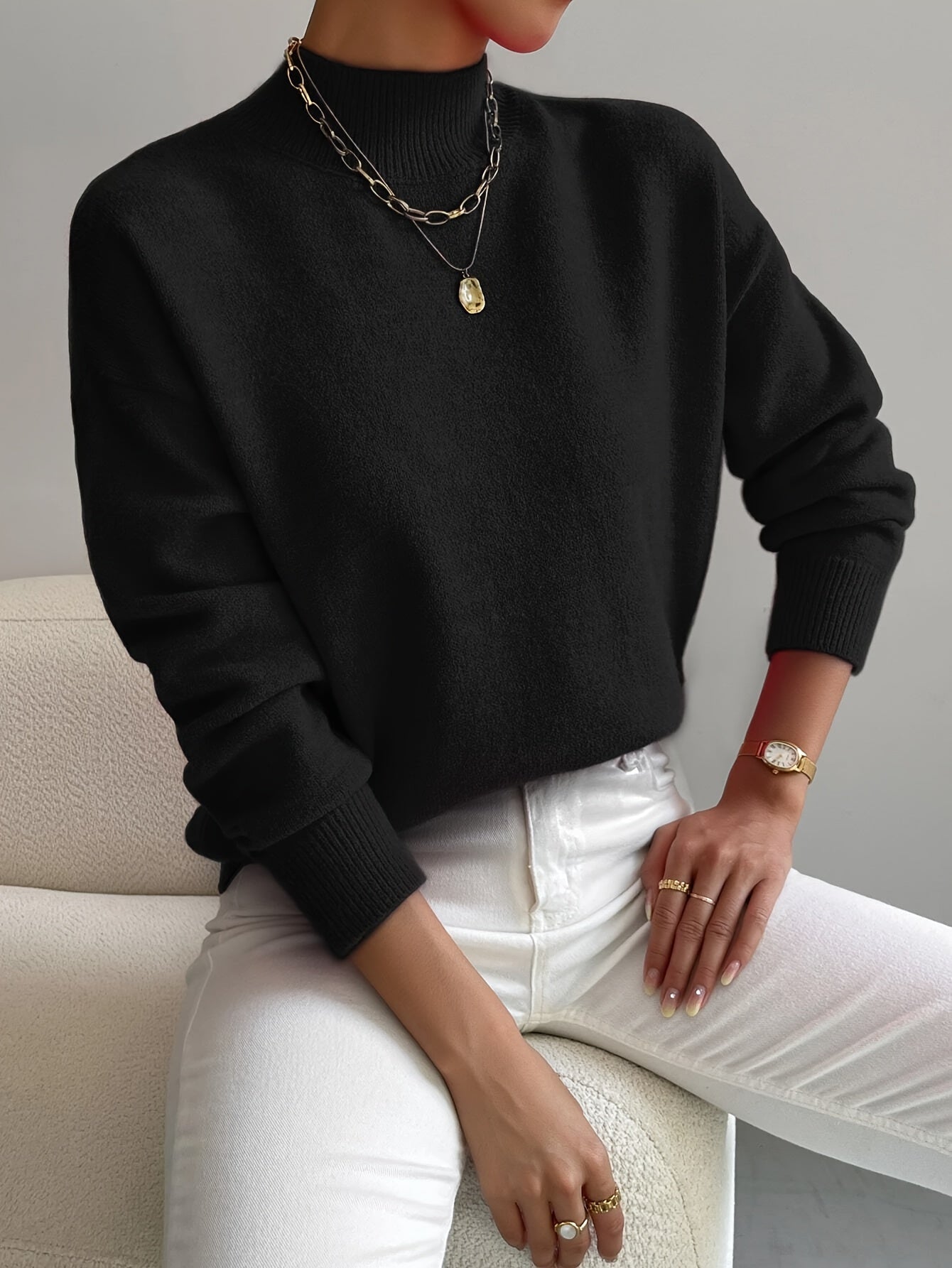 Black ribbed knit turtleneck sweater with dropped shoulders, long sleeves, and fitted cuffs worn with white jeans.