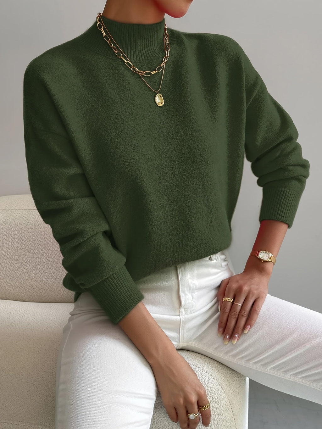 Olive green knit turtleneck sweater with a relaxed dropped-shoulder fit, ribbed cuffs, and hem worn with white jeans.