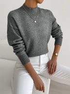 Grey ribbed turtleneck sweater with a relaxed dropped-shoulder fit, styled with white trousers.