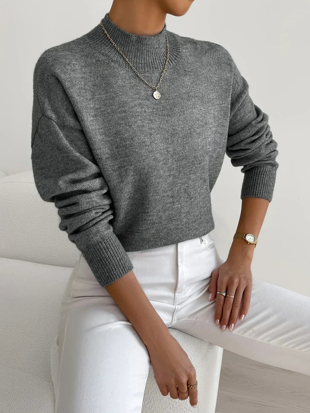 Grey ribbed turtleneck sweater with a relaxed dropped-shoulder fit, styled with white trousers.