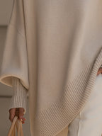 Beige oversized ribbed knit sweater with a loose poncho silhouette, long cuffed sleeves, and a soft, smooth texture.