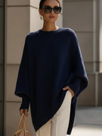 Navy blue oversized ribbed knit sweater with a loose poncho silhouette, long cuffed sleeves, and a high-low hem.