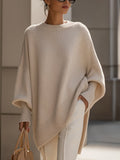 Oversized beige ribbed knit sweater with a loose poncho silhouette, wide sleeves, and structured cuffs worn with trousers.